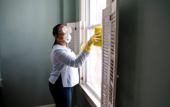 Mulher limpando a janela com equipamentos de proteção individual