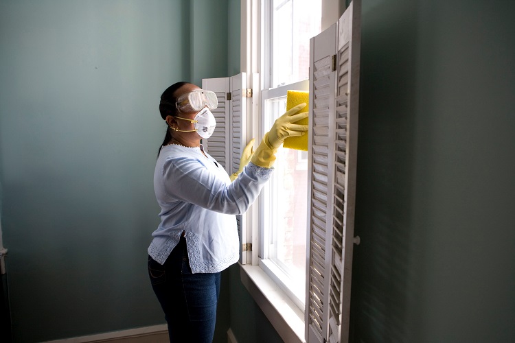 Mulher limpando a janela com equipamentos de proteção individual